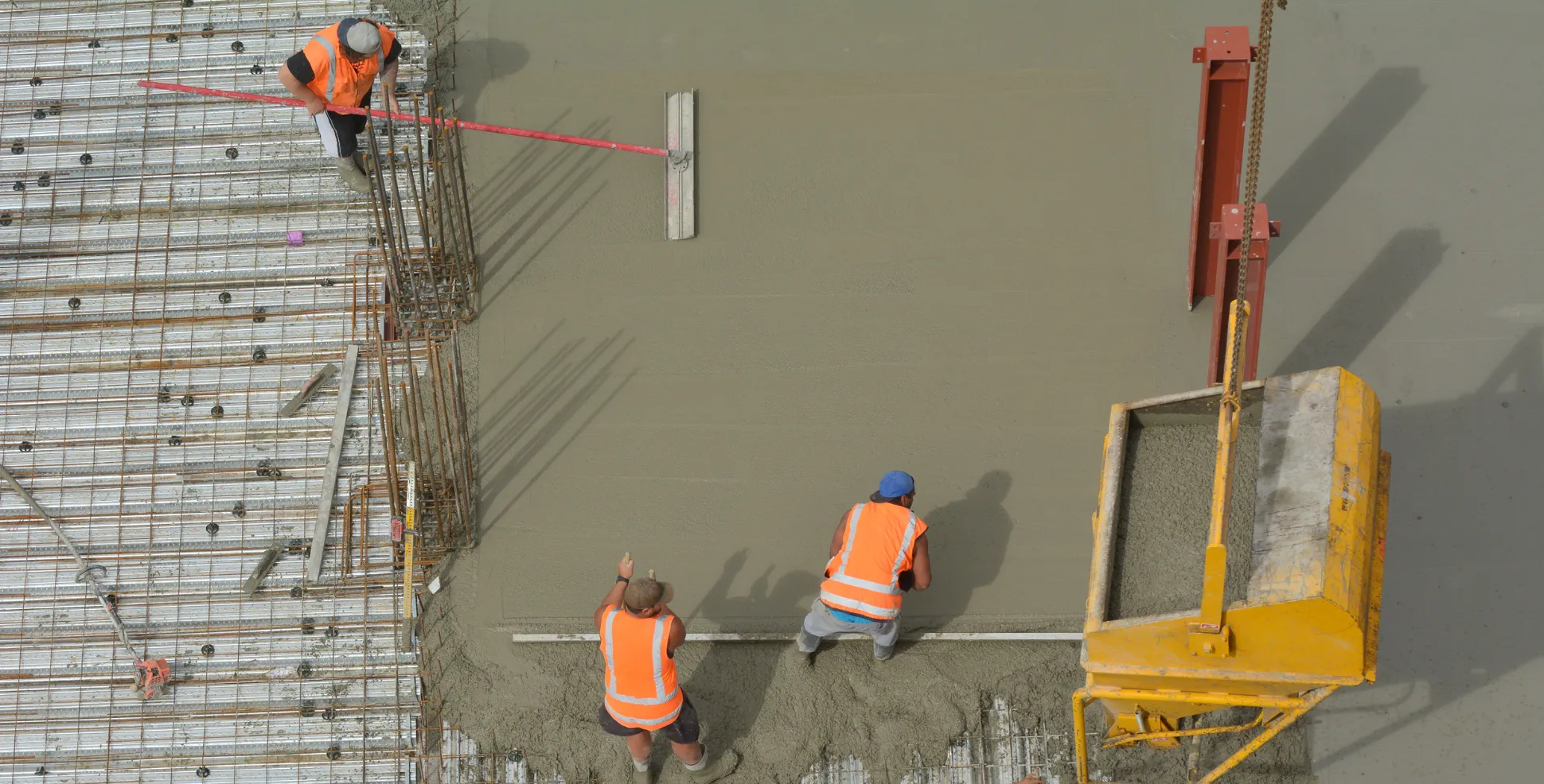Crew placing and leveling structural concrete over rebar reinforcement on commercial slab