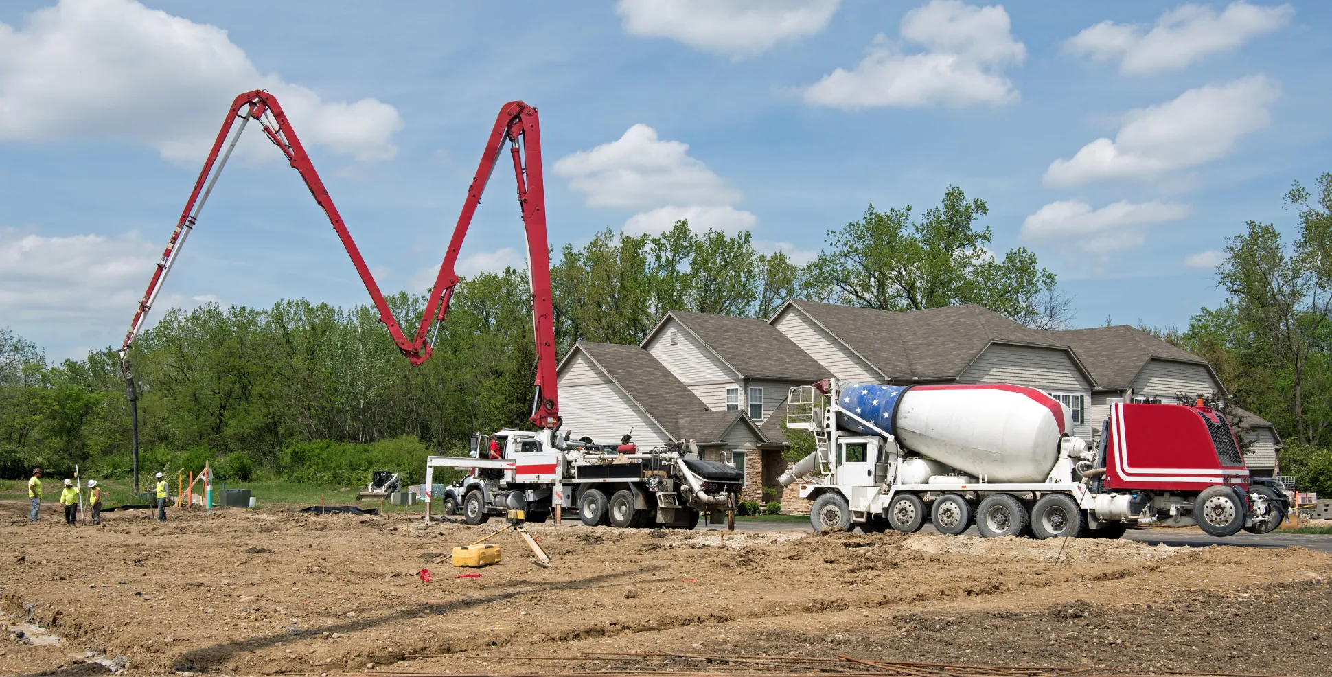 Concrete pump truck pouring foundation footings on active construction site with workers guiding placement