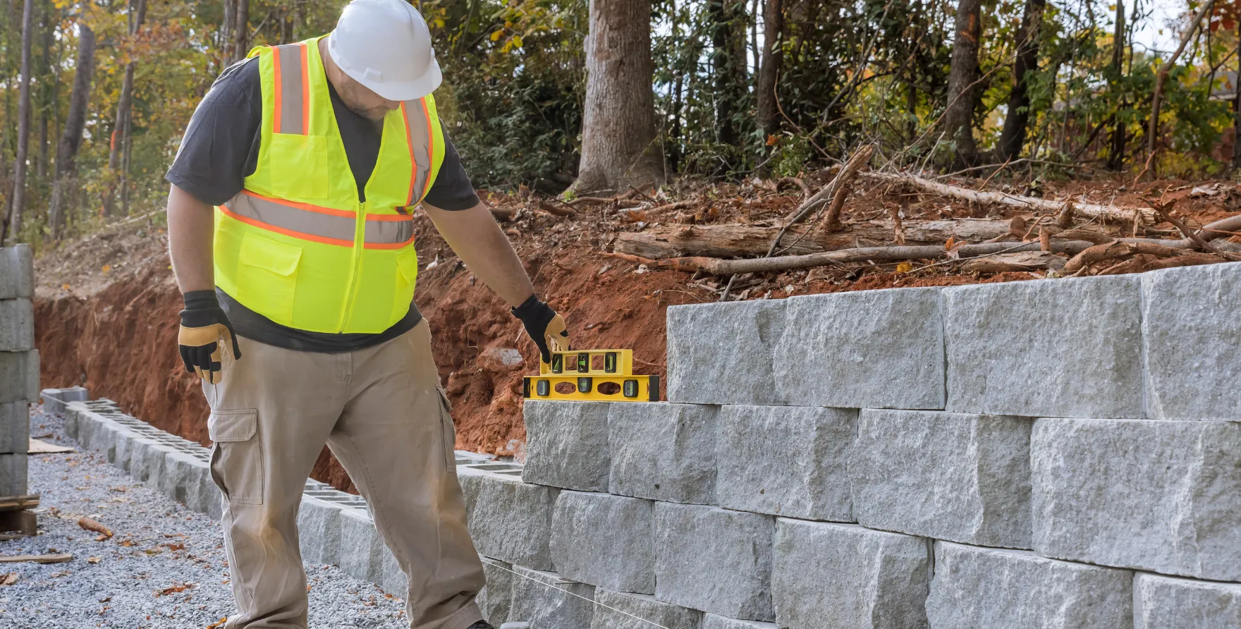 Worker leveling retaining wall blocks during construction to ensure perfect alignment