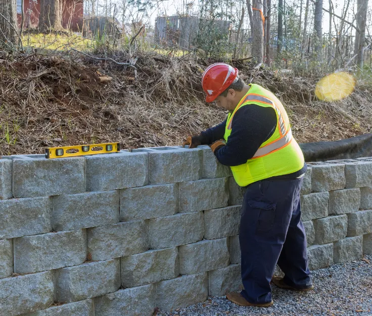 Worker leveling and aligning concrete wall blocks during retaining wall installation